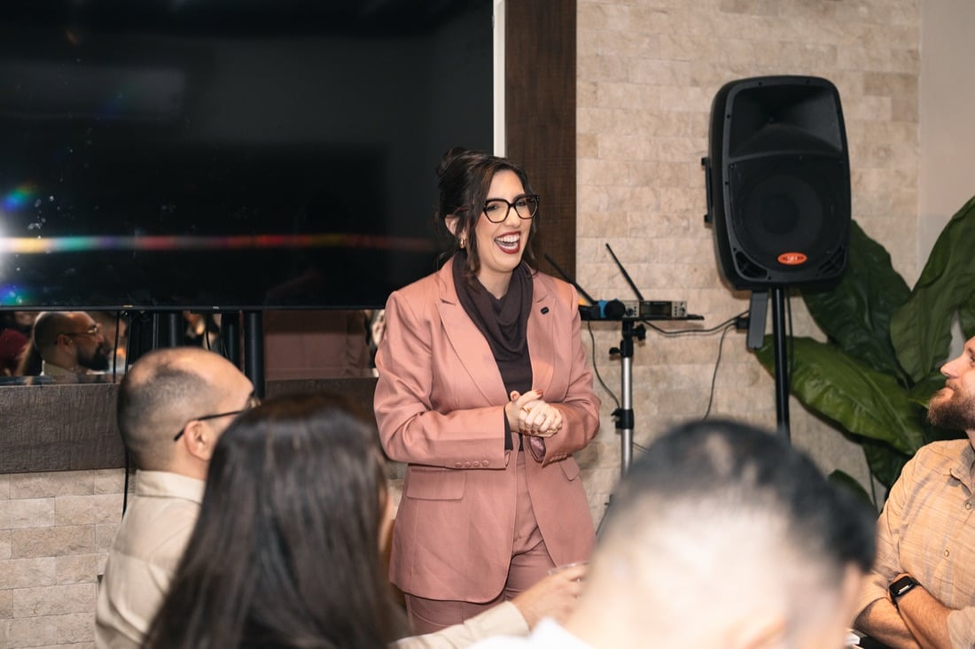 Lilian Cidreira sorrindo durante a palestra, diante dos convidados sentados à mesa